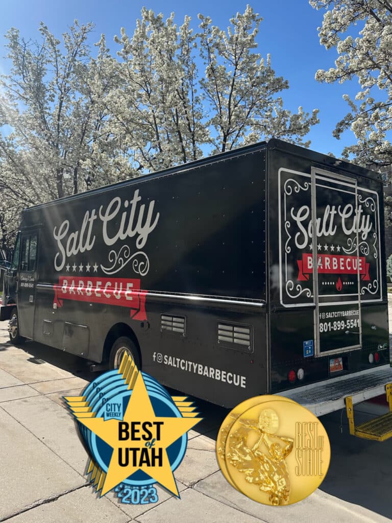Salt City Barbecue food truck parked under blooming white trees, decorated with ‘Best of Utah 2023’ and ‘Best in State’ award badges.
