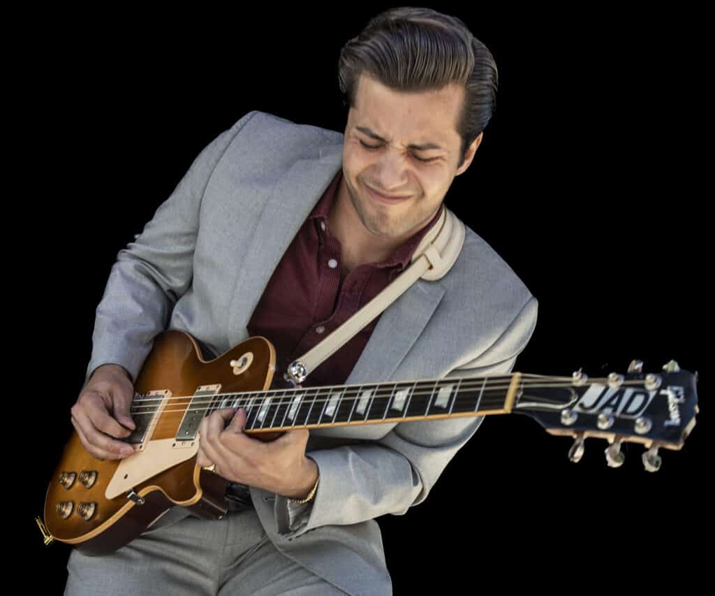 Jad Tariq passionately playing an electric guitar while wearing a light gray suit and a maroon shirt, his expression reflecting deep emotion during the performance.